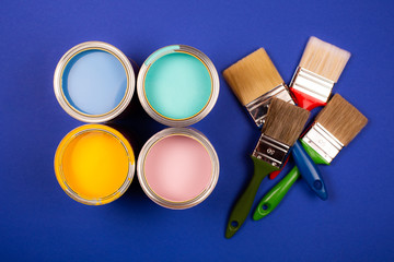 Four open cans of paint with brushes on blue background. Yellow, blue, pink, turquoise colors of paint. Top view.