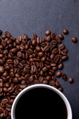 Roasted coffee beans and cup of coffee on granite background