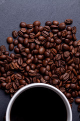 Roasted coffee beans and cup of coffee on granite background