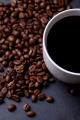 Roasted coffee beans and cup of coffee on granite background