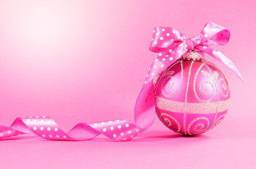 Pink festive bauble ornament with polka dot ribbon on a feminine pink background with copy space for Merry Christmas or Happy Holidays seasons greetings. Lens flare.