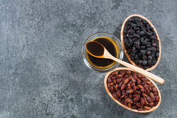 grape molasses in glass bowl , in wooden spoon and dried black and green grapes on rustic background, healthy food