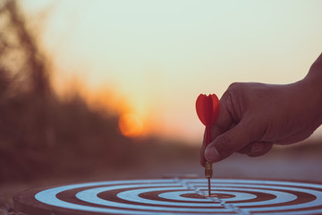 Close up hand hitting red arrow to target dartboard at sunset background. Business targeting and...