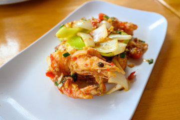 Fried prawns stir fried with chilies and salt, put onions and bell peppers in a white plate on an orange wooden table.