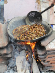 Traditional process of making roasted coffee bean menggoreng kopi. roasting beans in big pan on a wood-burning stove with firewood stir with large aluminum scoop utensil. Turn green seeds into black.