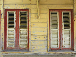 Rusted red and white windows over yellow facade. Tropical construction. Martinique, Antilles....