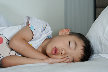 The lovely young Asian kid is lying and sleeping on the bed tightly
