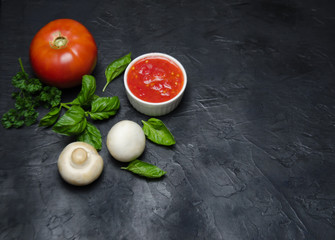 red tomato and mushrooms championsa near greens Basil lie with a Cup of sauce on a black background