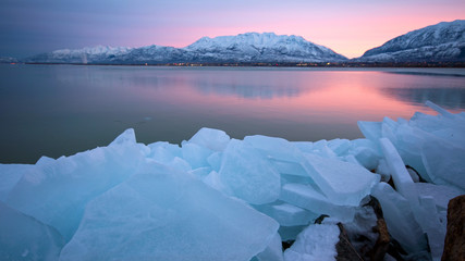Pink sunrise over lake with frozen ice blocks in a pile on the shore looking towards the snow...