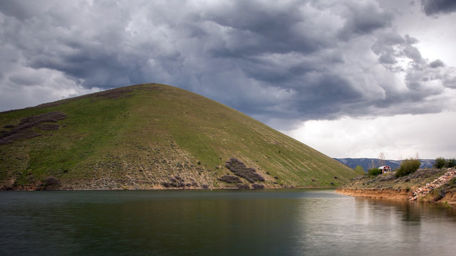 Thick dark clouds over Deer Creek Reservoir past grassy green hill in Utah.