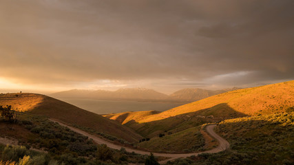 Looking towards Timpanogos Mountain at sunset as strong wind blasts through the canyon with winding dirt road looking towards Utah Lake.