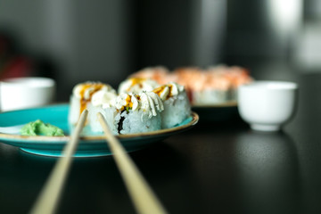 Fresh Asian sushi rolls with seafood and cream on a blue plate and on a black table with a white gravy boat and bokeh sticks side view. Sushi menu. Japanese food.