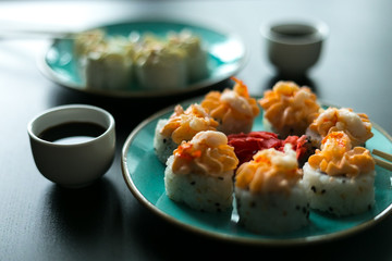 Cream sushi rolls with soy sauce ginger and wasabi on a black table and blue plates with chopsticks