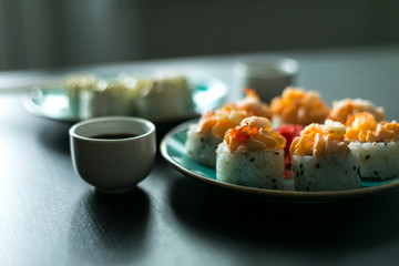 Cream sushi rolls with soy sauce ginger and wasabi on a black table and blue plates with chopsticks
