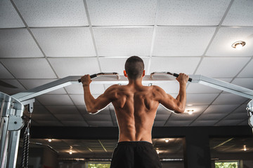 A young athlete trains his back muscles on a horizontal bar with a wide grip. Classes in the gym,...