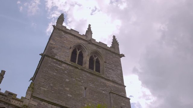 A low-angle, medium shot of the finials and double arched windows of a tall Gothic tower made of bricks and stones.
