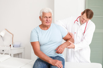 Doctor examining mature man with joint pain in clinic