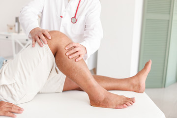 Doctor examining mature man with joint pain in clinic