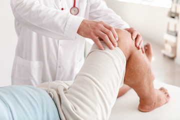 Doctor examining mature man with joint pain in clinic