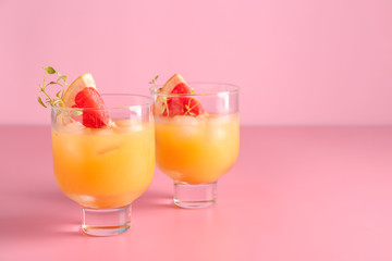 Glasses of fresh citrus juice on color background