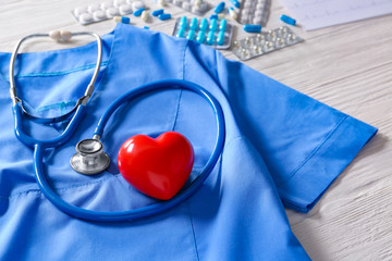 Stethoscope, doctor's uniform, heart and pills on wooden background. Cardiology concept