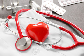 Stethoscope, doctor's uniform, heart and pills on grey background. Cardiology concept
