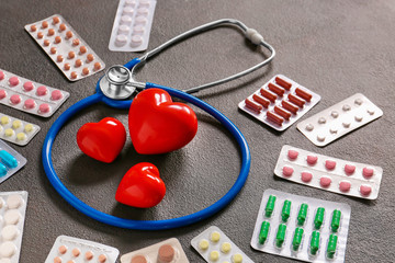 Stethoscope, hearts and pills on grey background. Cardiology concept