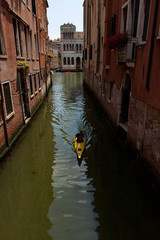 Fototapeta na wymiar Person in Kayak Paddling Through Canal in Venice
