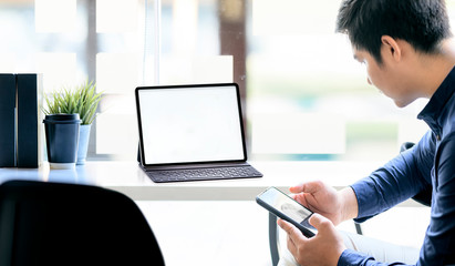 Cropped of businessman using smartphone and working with tablet while sitting at office desk in...