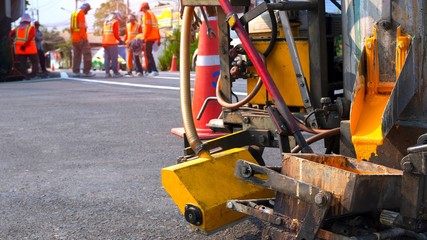 Fototapeta premium Close up thermoplastic spray marking machine with blurred background of road workers team discussing work on asphalt road in the city