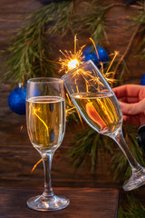 Glasses of champagne with bubbles on the background of Christmas decorations. Two glasses touch each other during a festive toast and sparklers burn beautifully. Beautiful card.