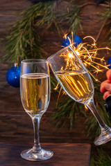 Glasses of champagne with bubbles on the background of Christmas decorations. Two glasses touch each other during a festive toast and sparklers burn beautifully. Beautiful card.