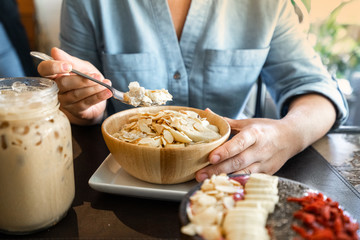 Female hands with a spoon in a cafe oatmeal breakfast with banana and almonds on coconut milk. Healthy breakfast.
