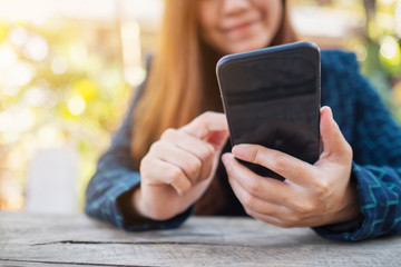 Closeup image of a woman holding , using and looking at mobile phone in the outdoors