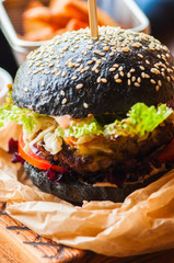 Black burger in a parchment paper on a wooden board.