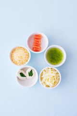Food ingredients for pizza in a small bowls on a blue background.