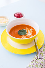 Carrot cheese soup with parsley in yellow bowl, blue background.