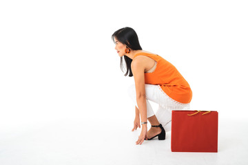 A beautiful Asian young woman wearing orange dress holding a start running position with a red shopping bag.