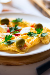 Fluffy french omelette with herbs, olives and feta cheese in a plate.