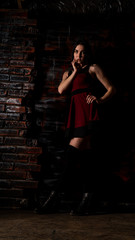 Fototapeta na wymiar Pretty young sexy model female with dark hair in amazing long red dress and black shoes posing in dark studio