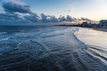Obraz premium Evening beach at Cape Greco. Sea with waves and sky in clouds, houses in the background. Cyprus