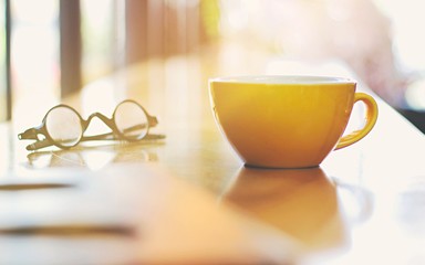 Cup of coffee, book and glasses on the wooden table, cozy home interior background