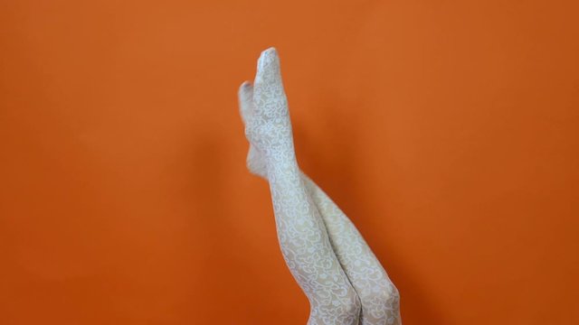 White fishnet stockings on perfect woman legs over bright orange background in studio