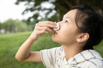 Sick asian child girl using tissue paper for stop bleeding from the nose,female teenage with nosebleed or epistaxis suffer from allergic rhinitis,respiratory or nose injury, bleeding from an accident