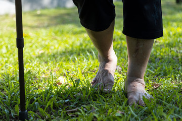 Closeup of barefoot feet,asian senior woman walking barefoot on grass in sunny summer,elderly female people with walking stick, relax and exercising in nature alone in the morning, healthy lifestyle
