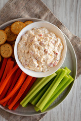 Top view, homemade Pimento Cheese Dip with carrots, celery and crackers over white wooden background. Flat lay, overhead, from above. Close-up.