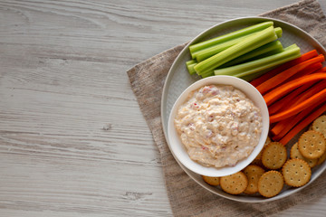 Top view, homemade Pimento Cheese Dip with carrots, celery and crackers over white wooden background. Flat lay, overhead, from above. Copy space.