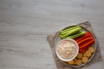 Homemade Pimento Cheese Dip with carrots, celery and crackers over white wooden surface, top view. Flat lay, overhead, from above. Space for text.