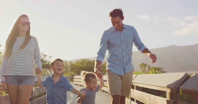Happy smiling family walking outdoors together at sunset, young toddler boys running outside with their parents, multi ethnic parents taking their children for a walk at sunset