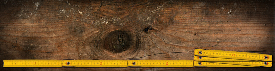 Close-up of a yellow wooden folding ruler on a work table with copy space and dark shadows